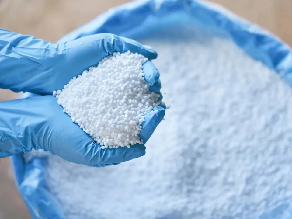 Gloved hands holding white urea granules